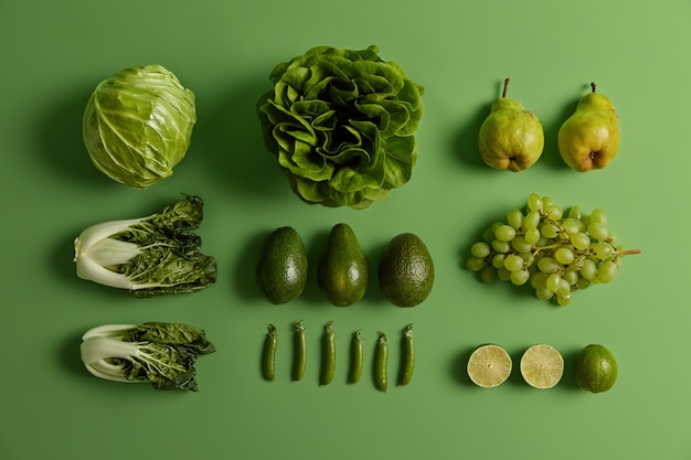 明るい緑の背景に新鮮な野菜や果物。熟した洋ナシ、ブドウ、ライム、キャベツ、レタスサラダ、エンドウ豆、チンゲン菜で健康的な食事を。クリエイティブなレイアウト。食料品および有機製品。