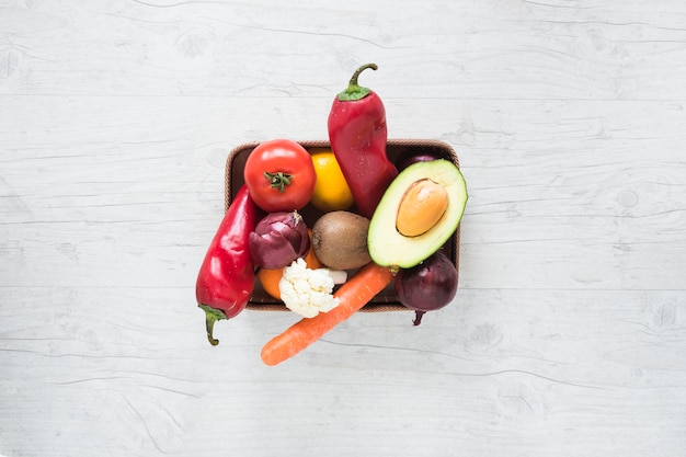 Fresh vegetables and fruits in container on white wooden backdrop