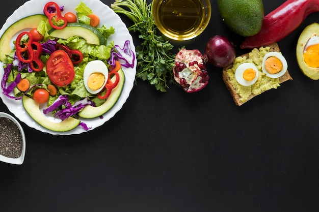 Foto gratuita insalata di verdure fresche; pane tostato; frutta; olio su sfondo nero