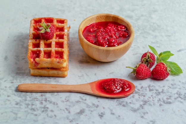 Fresh waffle with raspberry jam on grey surface.