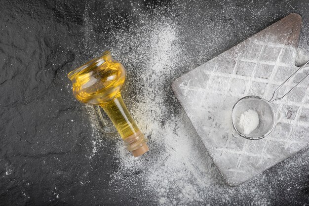 Fresh wheat floor spilled on wooden board with glass of oil