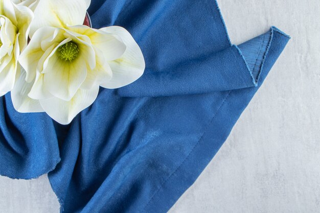 Fresh white flowers in a glass on a piece of fabric, on the white table.