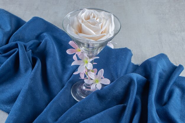 Fresh white flowers in a glass on a piece of fabric, on the white table.