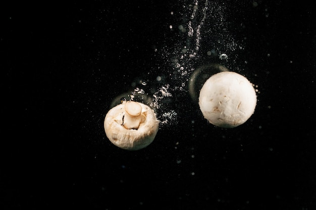 Funghi bianchi freschi cadono in acqua su sfondo nero