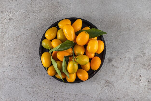 Fresh whole citrus cumquat fruits with leaves placed in black bowl.