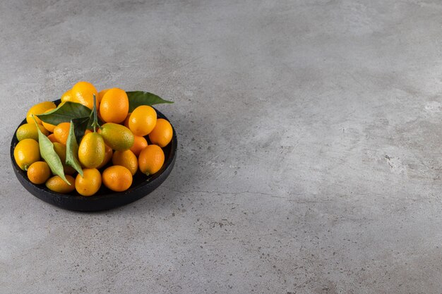 Fresh whole citrus cumquat fruits with leaves placed in bowl . 