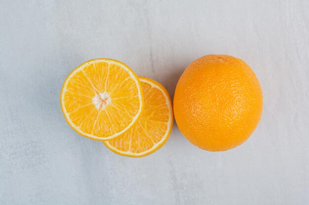 Свежие апельсины целиком и наполовину нарезанные на каменном фоне. Фото высокого качества