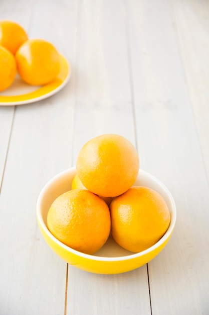 Fresh whole oranges in bowl and plate on wooden desk