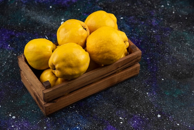 Free photo fresh whole quince fruits in wooden box on dark table.