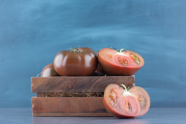 Свежие целые и нарезанные помидоры в деревянном ящике.