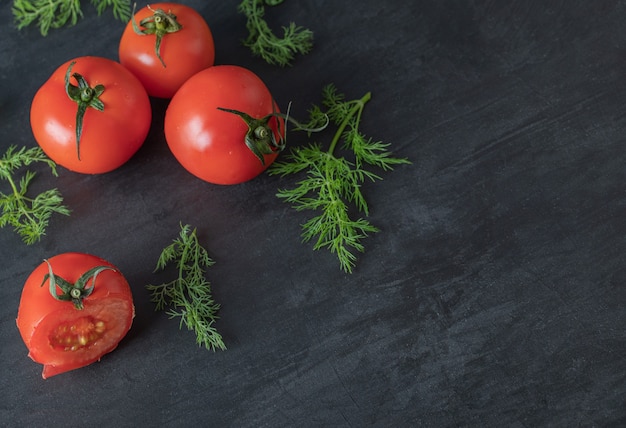 Fresh whole tomatoes with greens on a dark background. 