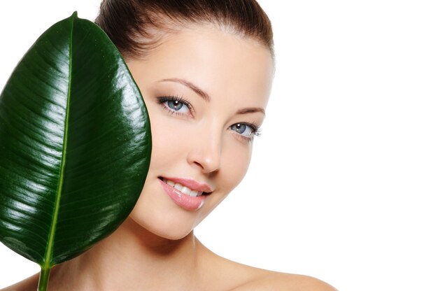 Fresh woman's face with cheerful smile and large green leaf over white backgrouns