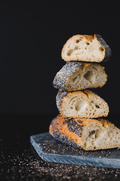 Freshly baked bread stacked on slate against black background