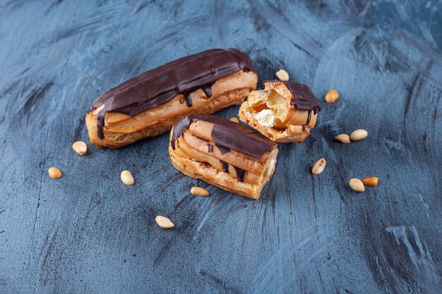 Freshly baked crispy chocolate eclairs with nuts placed on a colorful surface .