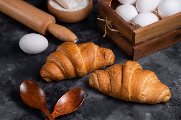 Freshly baked croissants with chicken eggs and kitchen utensils .