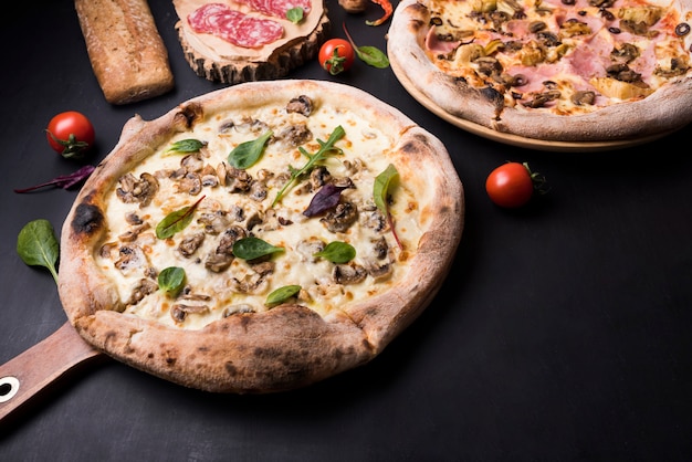 Свежеиспеченная итальянская пицца; пепперони и помидоры черри на черной поверхности