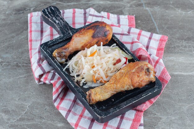 Freshly grilled chicken drumsticks and sauerkraut on black wooden board.