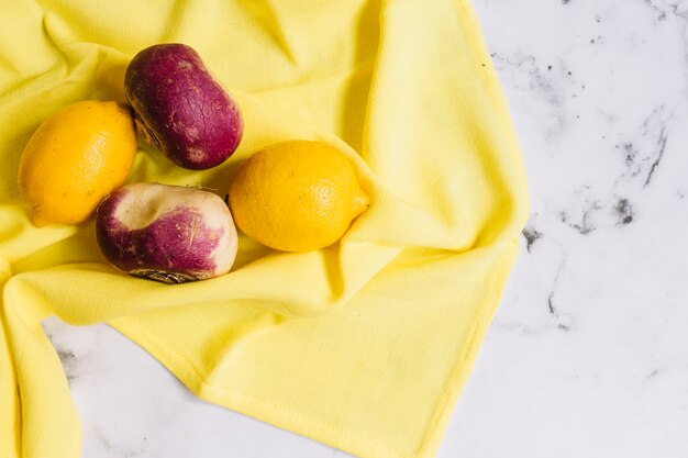 Freshly harvested spring turnips and lemons on yellow tablecloth against white marble backdrop