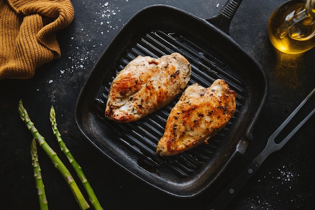 Fried appetizing tasty chicken breast served on skillet with asparagus Dark background