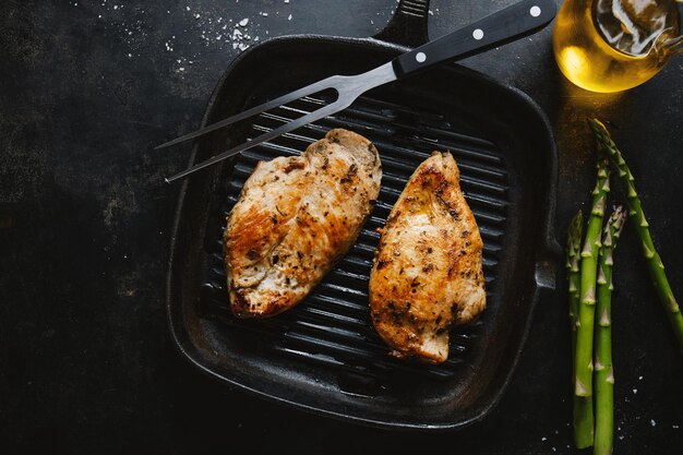 揚げた食欲をそそるおいしい鶏の胸肉をアスパラガスのフライパンで提供暗い背景