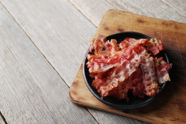 Fried bacon on black plate and wooden cutting board