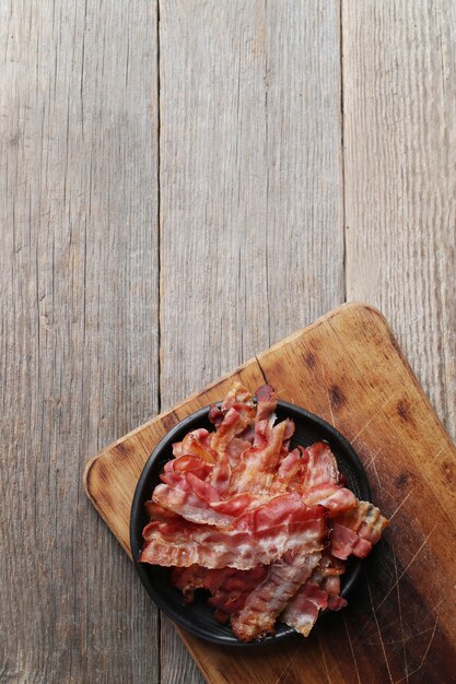 Fried bacon on black plate and wooden cutting board