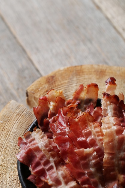 Free photo fried bacon on black plate and wooden cutting board