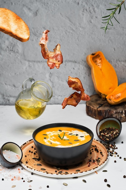 Free photo fried bacon slices, fried bread, rosemary fall into a bowl of pumpkin soup