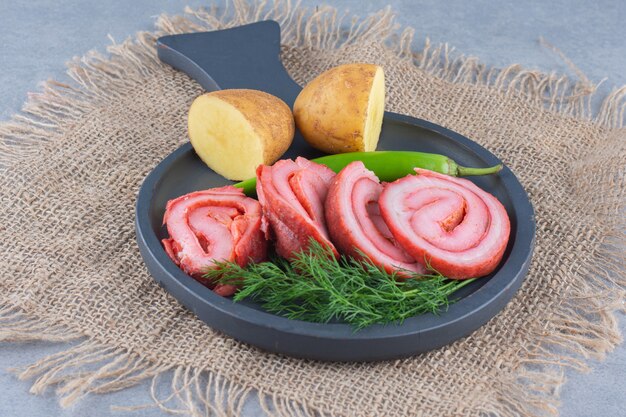 Fried bacons on black frying pan with vegetables. 