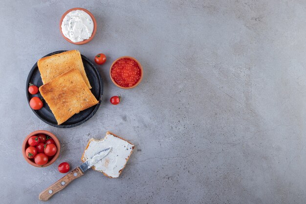 Fried bread with caviar and red cherry tomatoes placed on marble background.