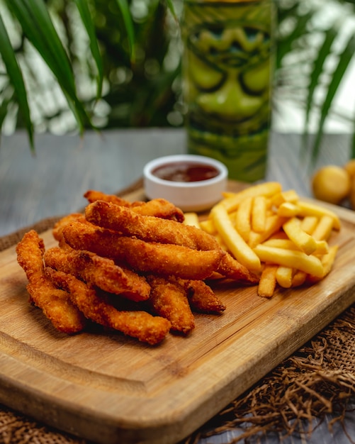 Foto gratuita strisce di petto di pollo impanate fritte con ketchup e patate fritte su un bordo di legno