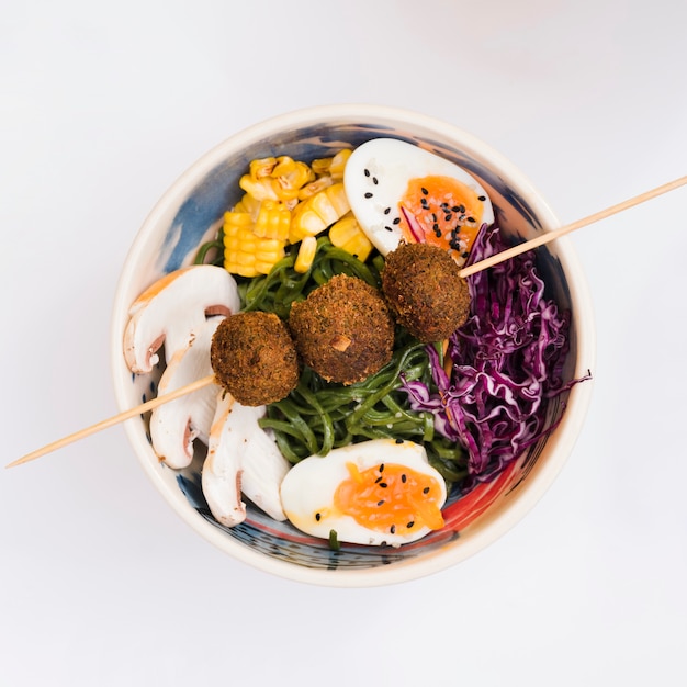 Fried chicken balls on stick over the bowl with mushroom; corn; egg; cabbage and seaweeds salad
