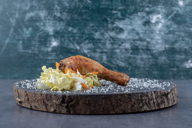 Жареная куриная голень и салат на деревянной доске.