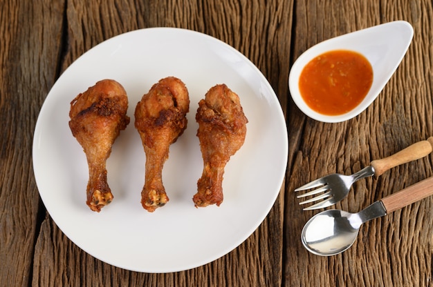 Fried chicken legs on a white plate with spoon, fork, and sauce.