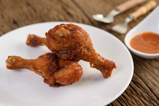 Fried chicken legs on a white plate with spoon, fork, and sauce.