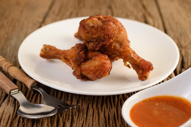 Fried chicken legs on a white plate with spoon, fork, and sauce.