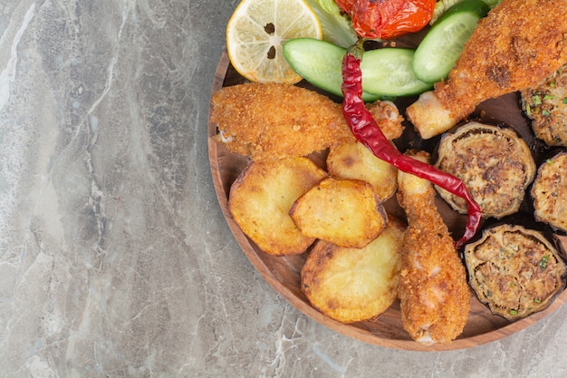 Free photo fried chicken legs with potato and eggplant on wooden board.