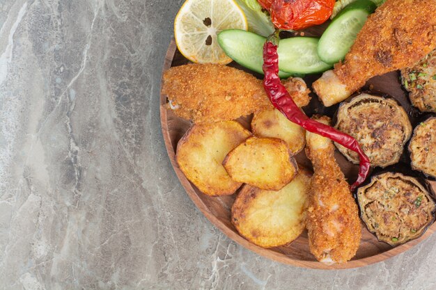 Fried chicken legs with potato and eggplant on wooden board.