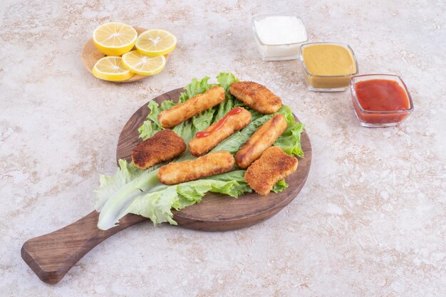 Fried chicken nuggets and grilled sausage sticks on a piece of lettuce with sauces around.