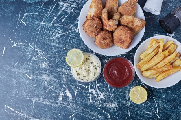 Fried chicken nuggets, legs and potatoes with sauces, top view.