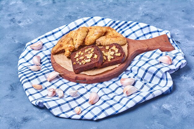 Fried chicken wings with dark bread on a wooden board on blue