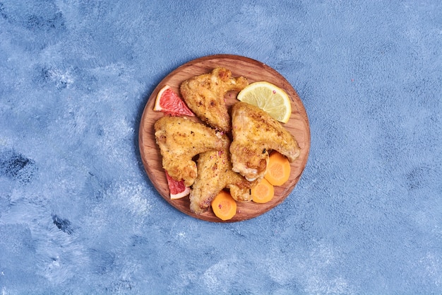 Free photo fried chicken wings on a wooden board on blue