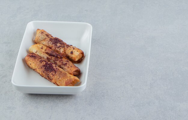 Fried cigar shaped pastries in white bowl. 