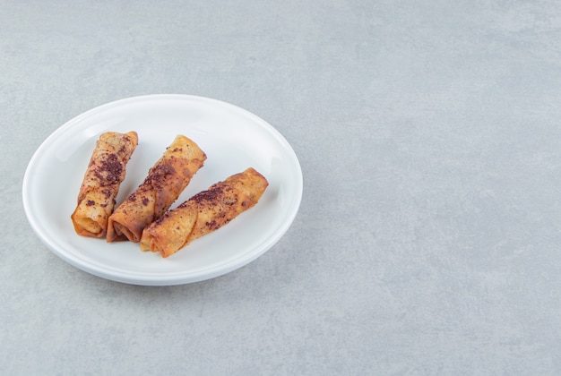 Fried cigar shaped pastries on white plate. 