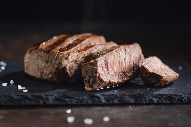 Fried cooked grilled meat with spices cut in slices served on dark slate Closeup