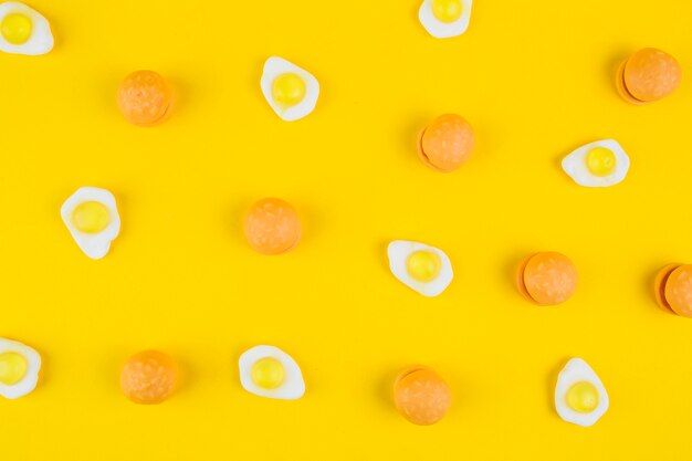 Fried egg gummies and burger candies on yellow background