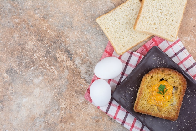 Fried egg inside toast on black plate with bread slices