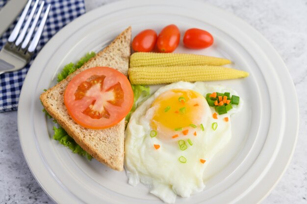 A fried egg laying on a toast, topped with pepper seeds with carrots, baby corn and spring onions.