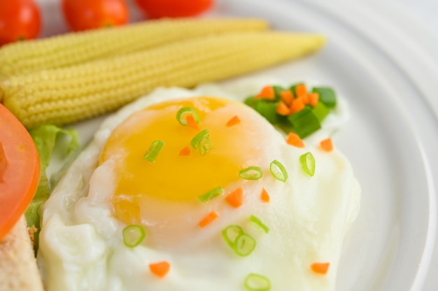 A fried egg laying on a toast, topped with pepper seeds with carrots, baby corn and spring onions.