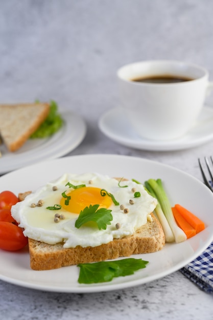 A fried egg laying on a toast, topped with pepper seeds with carrots and spring onions.